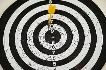 Close-up of a dart hitting the bullseye on a black and white target board symbolizing success. HD wallpaper