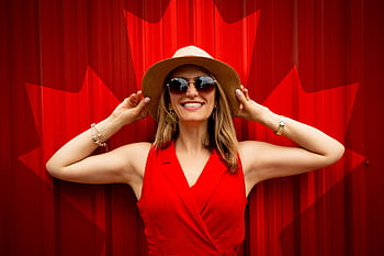 A fashionable woman in a red dress and hat smiling proudly in front of a Canadian flag backdrop. HD wallpaper