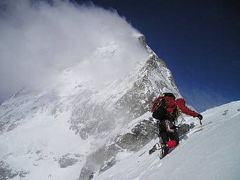 Thrilling adventure of a climber scaling a snowy mountain with dramatic clouds above. HD wallpaper