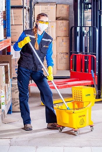 Female janitor in safety gear cleaning a warehouse floor with a mop and bucket. HD phone wallpaper
