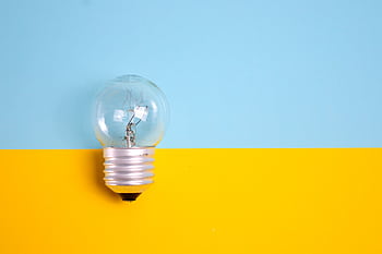 A clear light bulb against a vibrant blue and yellow background, symbolizing energy and creativity. HD wallpaper