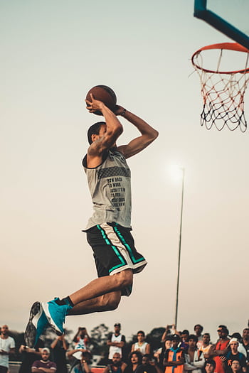 Athlete executing a powerful dunk during an intense outdoor basketball game. HD phone wallpaper