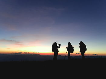 Group of hikers silhouetted against a vibrant sunset, enjoying an adventurous outdoor trek. HD wallpaper