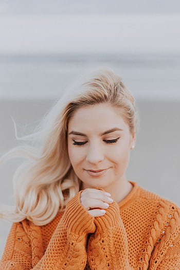 Blonde woman in knitted sweater enjoying a peaceful moment on a windy beach. HD phone wallpaper