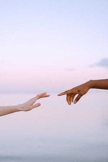 Two diverse hands reaching towards each other over a serene pastel sky and water background. HD phone wallpaper