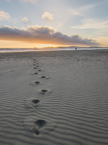 Tranquil beach scene at sunset with footprints leading to the horizon. HD phone wallpaper