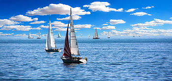Vibrant sailboats sailing under a clear blue sky with fluffy clouds. HD wallpaper