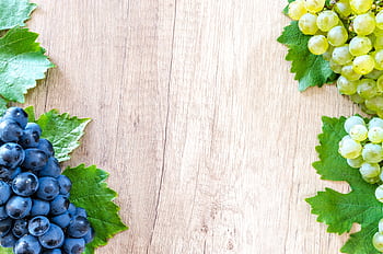 Clusters of fresh blue and green grapes with leaves on a wooden surface. HD wallpaper