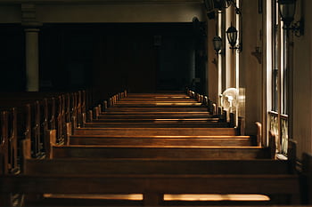 Serene church interior featuring wooden pews and beautiful lighting casting shadows through windows. HD wallpaper