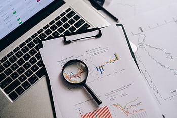 Overhead view of financial charts, laptop, and magnifying glass, ideal for business analysis themes. HD wallpaper