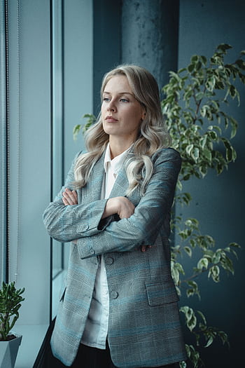 A poised female executive standing by a window, embodying leadership and professionalism. HD phone wallpaper