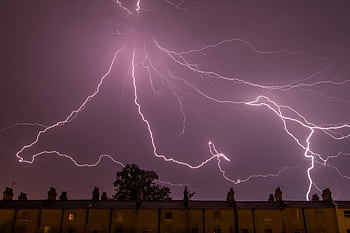 A captivating lightning storm illuminating the night sky above city rooftops. HD wallpaper