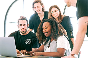 A diverse group of young professionals collaborating around a laptop in a modern office setting. Perfect for business or tech concepts. HD wallpaper