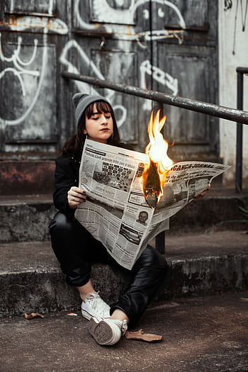 Woman sits outdoors reading a newspaper on fire, creating a dramatic urban scene. HD phone wallpaper