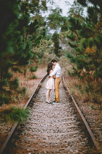 A romantic couple embracing on railway tracks surrounded by nature, depicting love and togetherness. HD phone wallpaper