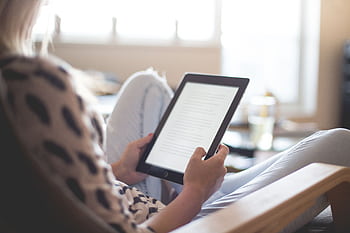 A woman enjoys reading on a tablet, sitting comfortably in a modern living room. HD wallpaper