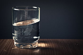 A clear glass of water sitting on a wooden table against a dark background. HD wallpaper