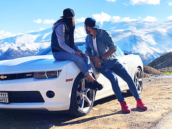 A young couple enjoys a scenic mountainous view while seated on a sports car. HD wallpaper