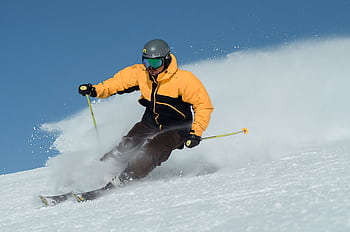 A focused skier wearing a bright jacket expertly navigating a snowy slope under clear skies. HD wallpaper