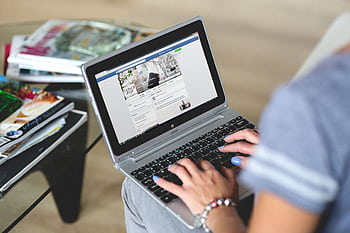 A woman typing on a laptop with social media on the screen, indoors setting. HD wallpaper