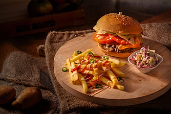 A mouthwatering cheeseburger with fresh fries and coleslaw on a rustic wooden board. HD wallpaper