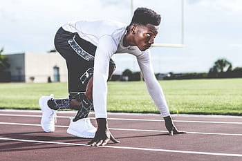 Focused athlete in starting position on a sunny track field, ready to sprint. HD wallpaper