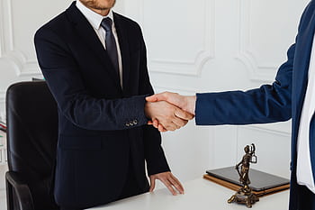 Two men in suits shaking hands in a formal office environment symbolizing an agreement. HD wallpaper