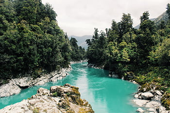 Beautiful turquoise river winding through a dense, lush forest under a cloudy sky. HD wallpaper