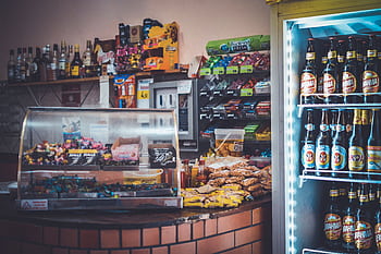 A well-stocked convenience store counter with snacks, drinks, and a refrigerator showcasing beverages. HD wallpaper