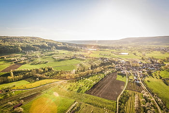 Scenic aerial view of a sunlit countryside village surrounded by green fields. HD wallpaper