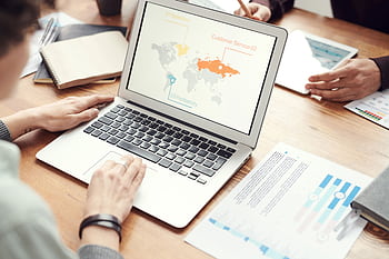 Professional team discussing global marketing strategies with charts and graphs on a laptop. HD wallpaper