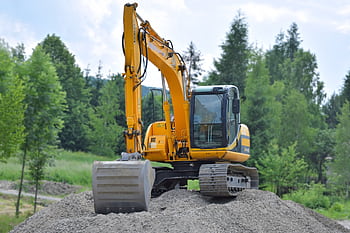 A yellow excavator on a pile of gravel in a lush, green forest setting in Poland. HD wallpaper