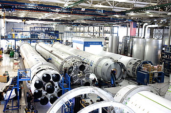 View of a spacecraft assembly line with rockets in a spacious hangar. HD wallpaper