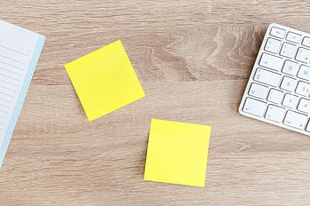 Flat lay of a workspace featuring yellow sticky notes, a keyboard, and a notebook on a wooden desk. HD wallpaper