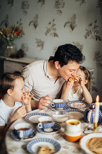 A father and his two children share a joyful meal featuring traditional crepes, creating a warm family moment indoors. HD phone wallpaper