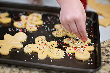 A close-up of gingerbread cookies being decorated with colorful sprinkles on a baking tray. HD wallpaper