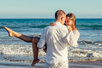 Young couple enjoying a romantic moment on a sunny beach, with waves in the background. HD wallpaper