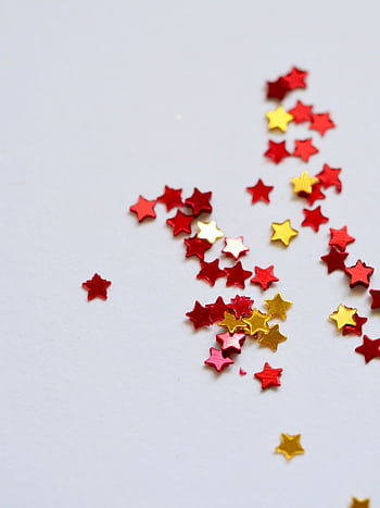 Vibrant red and gold star-shaped confetti scattered on a plain white surface, perfect for festive and celebratory themes. HD phone wallpaper