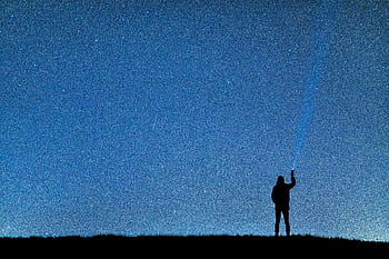 A person with a flashlight gazing at the stars, creating a silhouette against the night sky. HD wallpaper