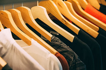 A close-up view of a row of clothes on wooden hangers, showcasing various fabrics and colors in a wardrobe setting. HD wallpaper