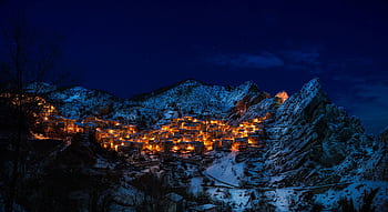 A captivating winter scene of a snow-covered mountain village illuminated at night. HD wallpaper