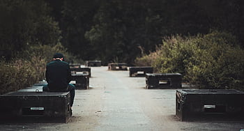 A man sitting alone on a bench along a concrete path in a serene outdoor setting. HD wallpaper