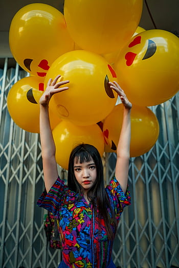 A young woman poses with bright emoji balloons against an urban background. HD phone wallpaper