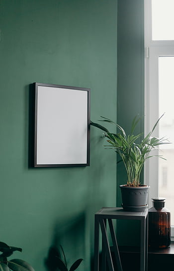 Stylish interior featuring a blank frame on a green wall and a potted plant by a window. HD phone wallpaper