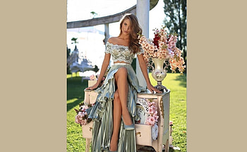 Brunette posing and sitting on a small table, blue vertical striped skirt, green grass, brunette, matching heels, off shoulder lace top, smoked glass vase with flowers HD wallpaper