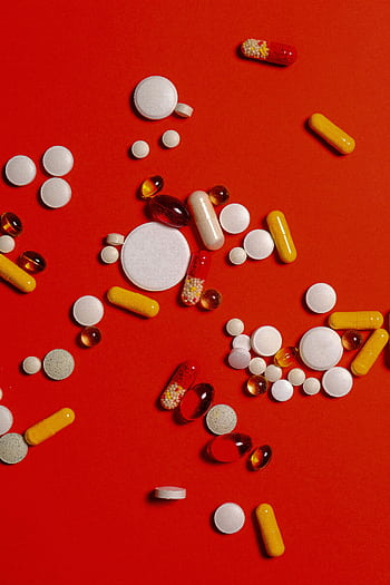 A diverse array of pills and capsules scattered on a vibrant red surface. HD phone wallpaper