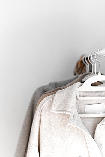 A selection of neutral-colored clothes hang neatly on white hangers against a plain backdrop. HD phone wallpaper