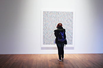 A woman with a backpack observes a colorful painting in an art gallery. HD wallpaper