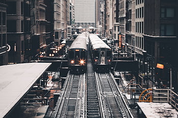 View of trains on elevated tracks in a busy downtown cityscape, showcasing urban transportation. HD wallpaper
