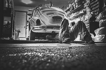 Mechanic working beneath a classic Volkswagen Beetle in a vintage garage setting. HD wallpaper